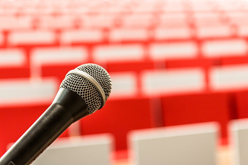 A photo of a microphone with empty red chairs in the background.